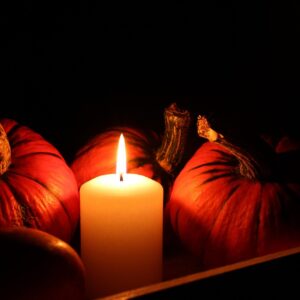 Calabaza de otoño junto a una vela encendida en un ambiente oscuro de Halloween